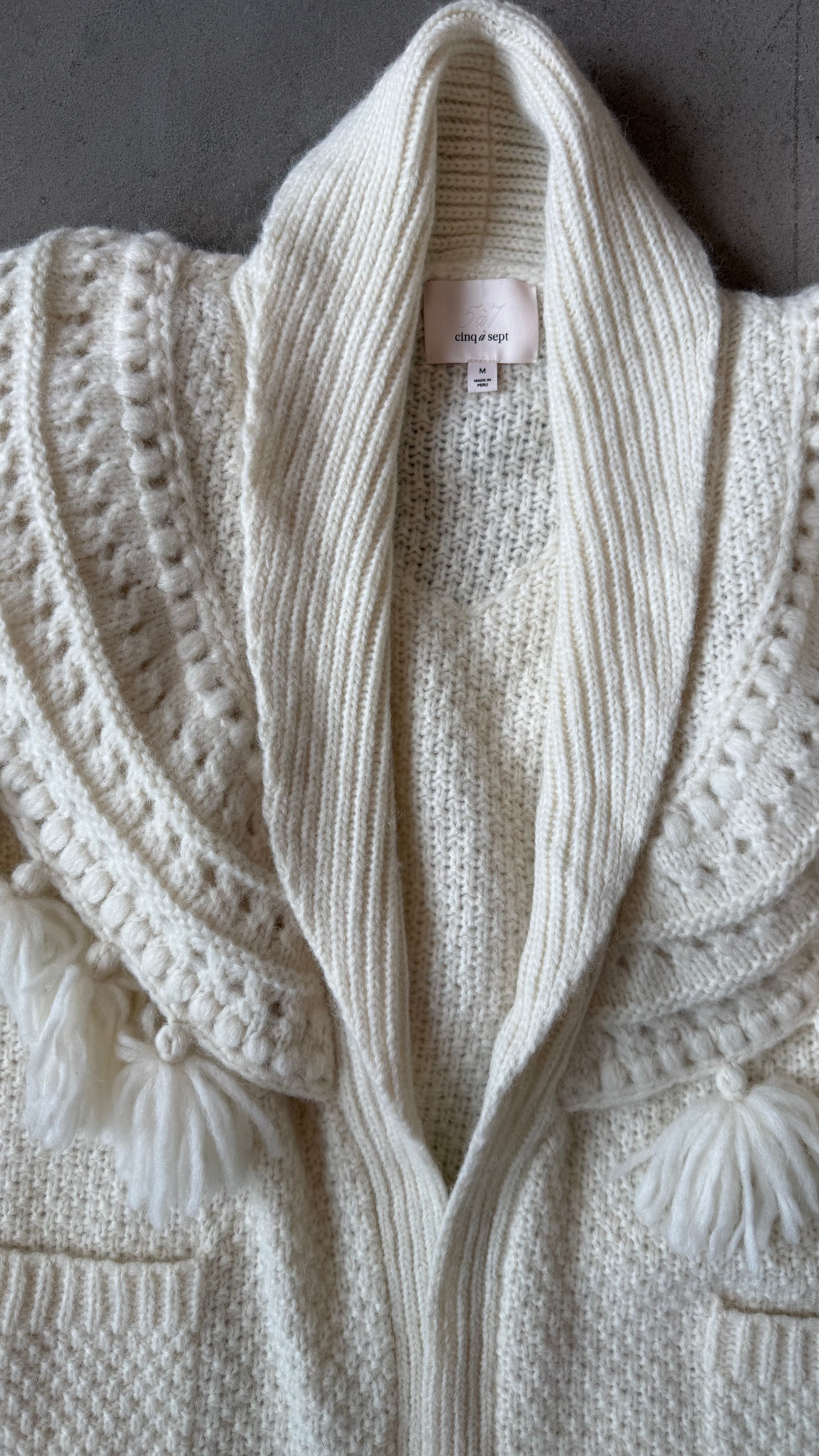 Close-up of a cream-colored knitted cardigan with a brand tag.