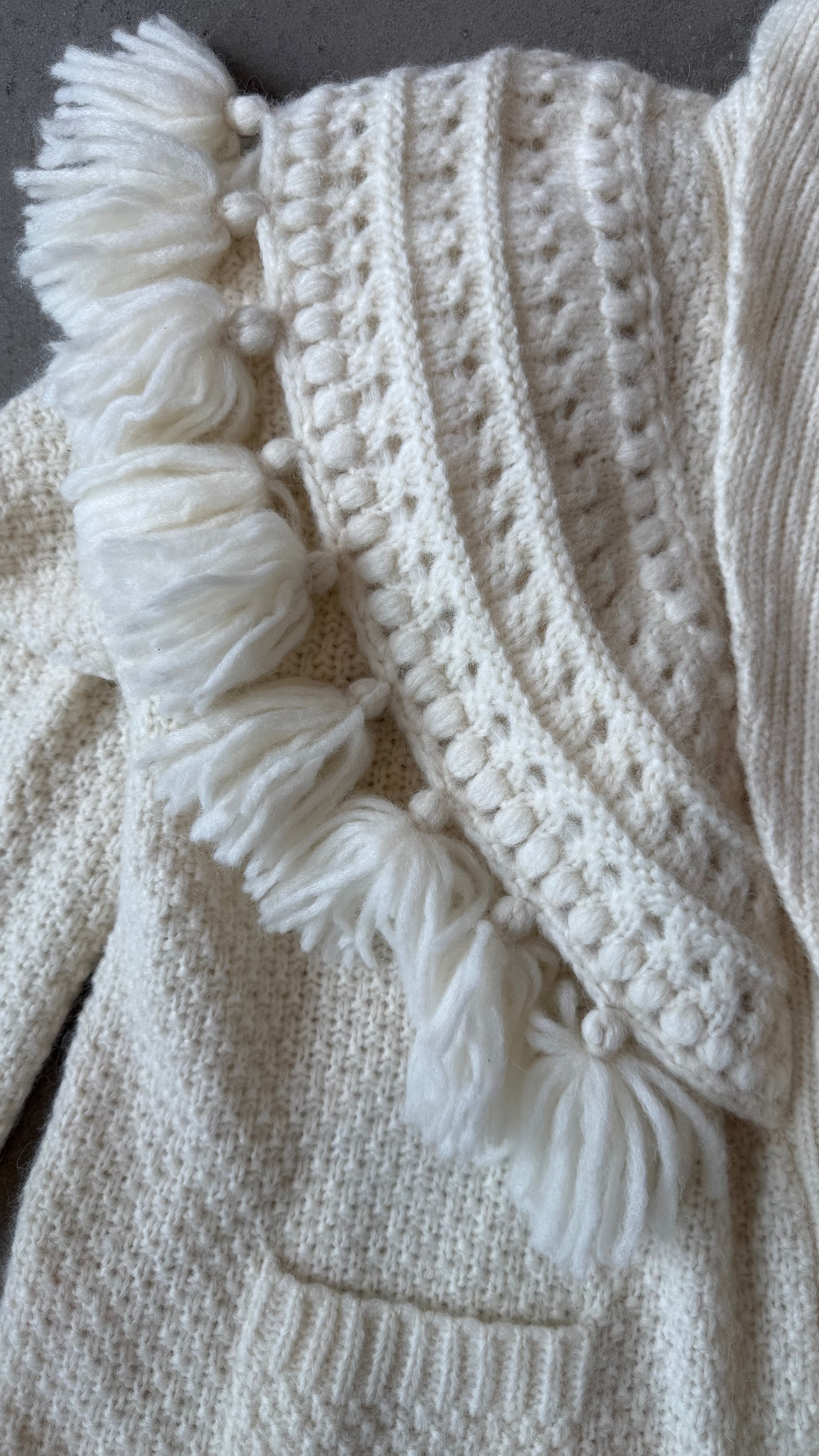 Close-up of a textured white knitted fabric with tassels and buttons.