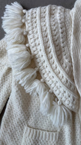 Close-up of a textured white knitted fabric with tassels and buttons.