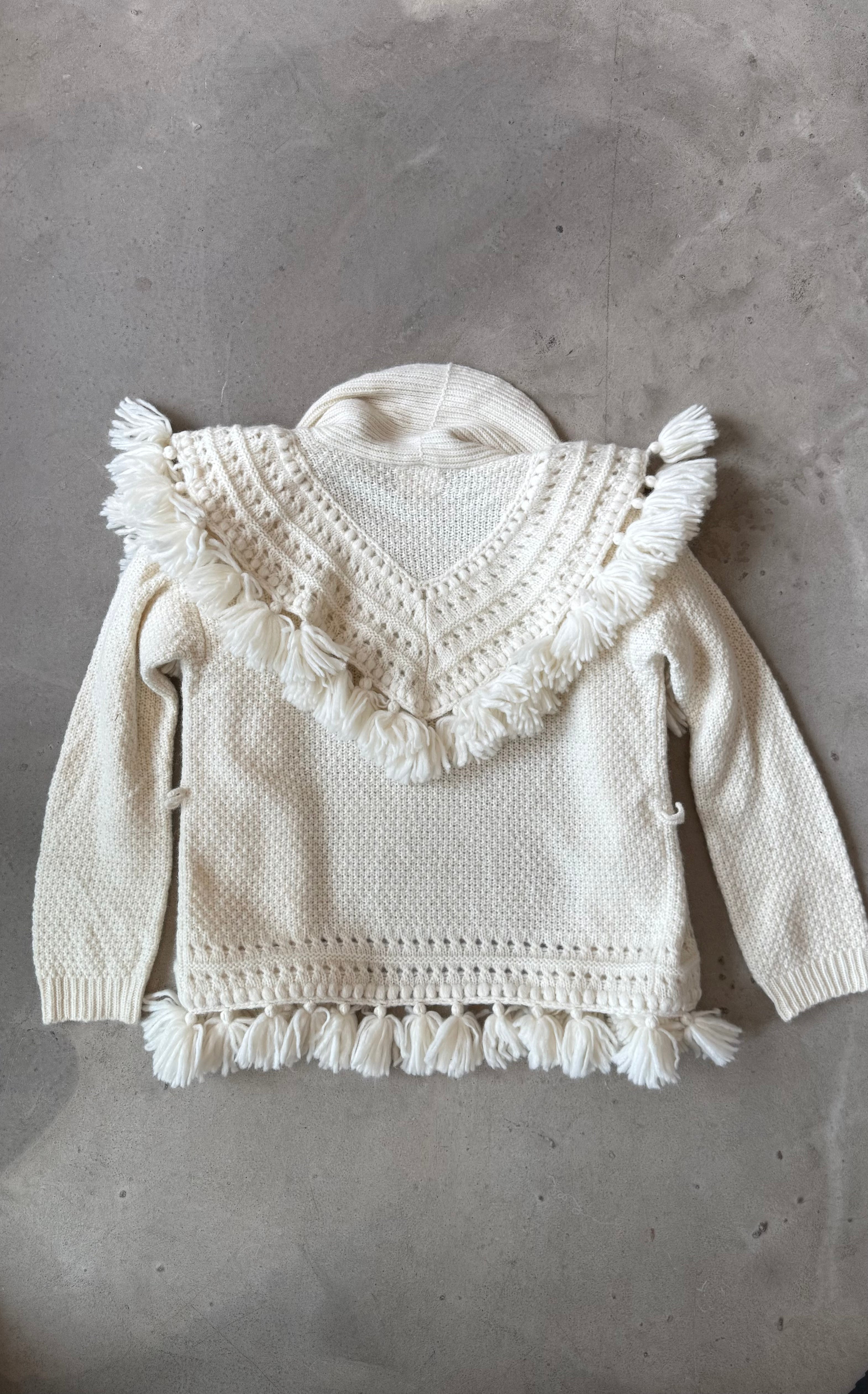 White knitted sweater with lace details and tassels on a gray surface