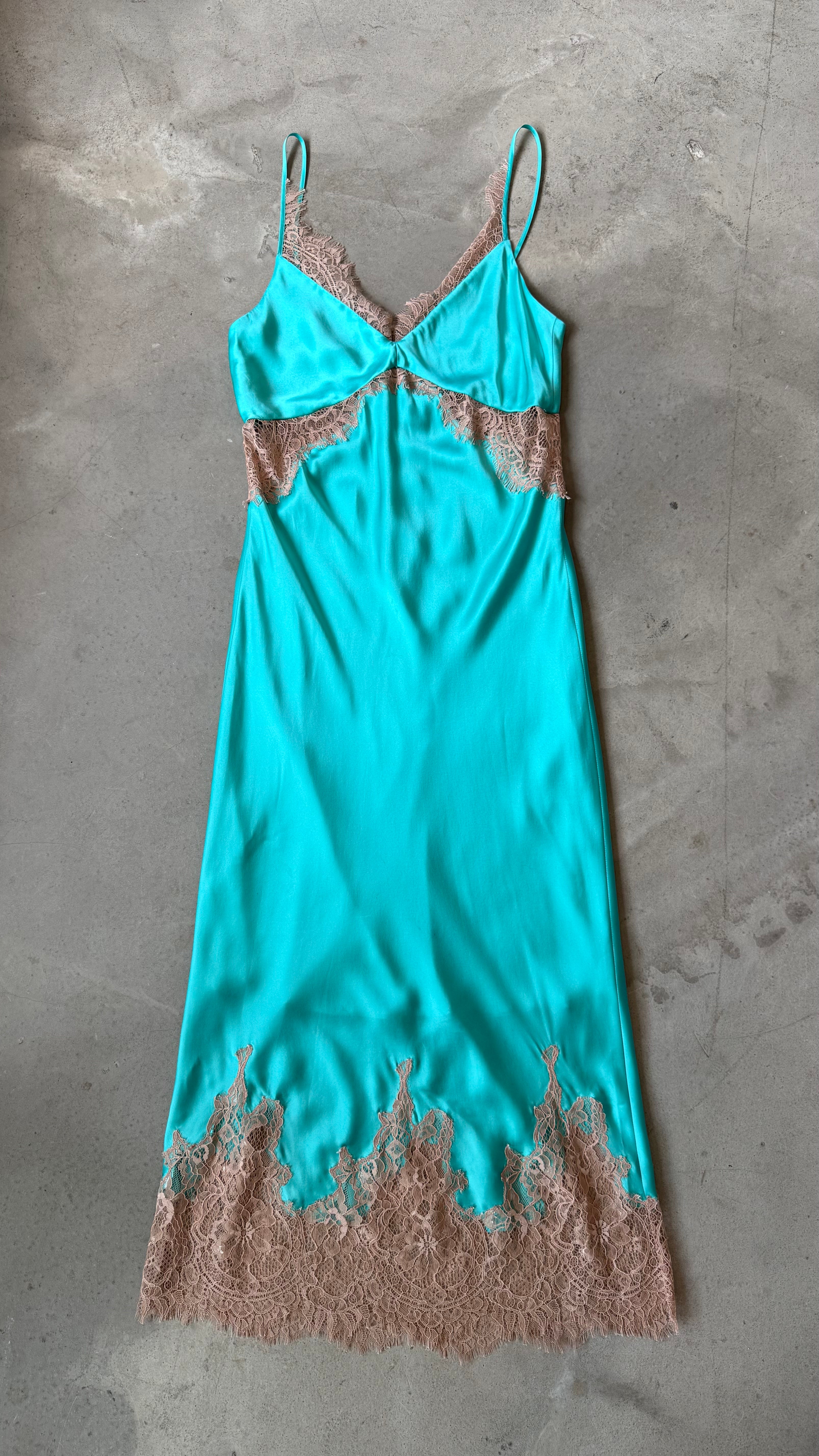 Turquoise slip dress with lace details on a gray concrete surface