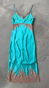 Turquoise slip dress with lace details on a gray concrete surface